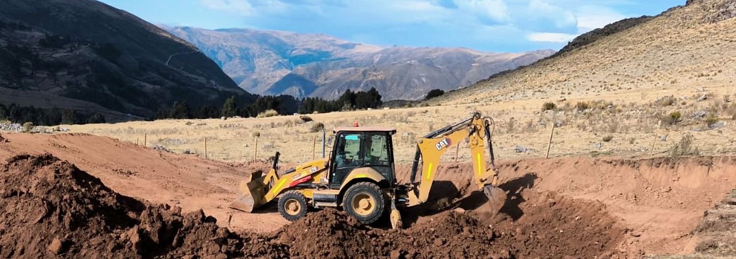 Retroexcavadora excavando una plataforma en tierra roja, con la cordillera al fondo