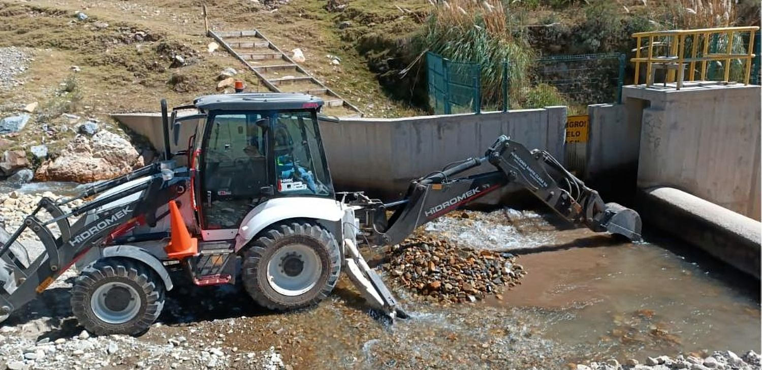 Retroexcavadora trabajando en un cauce junto a una estructura de concreto