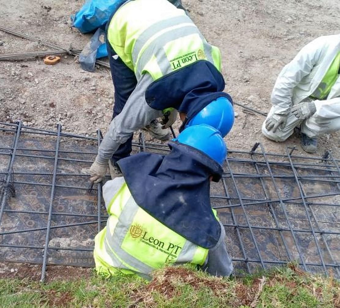 Dos trabajadores con chaleco de León PT amarran una malla de acero de refuerzo
