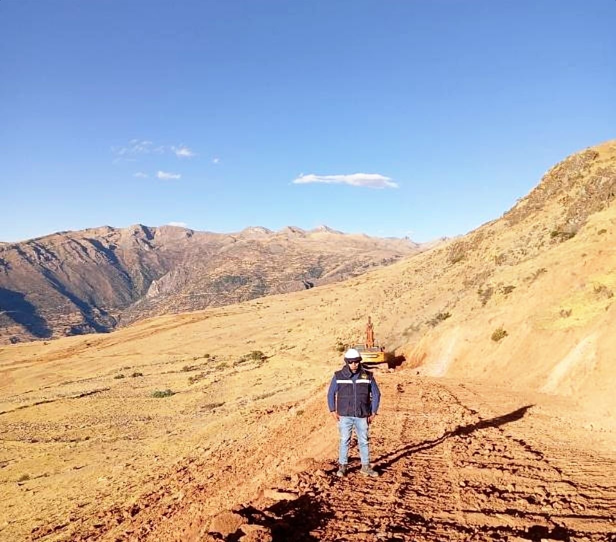Acceso recién conformado en tierra roja sobre una ladera, con la cordillera al fondo
